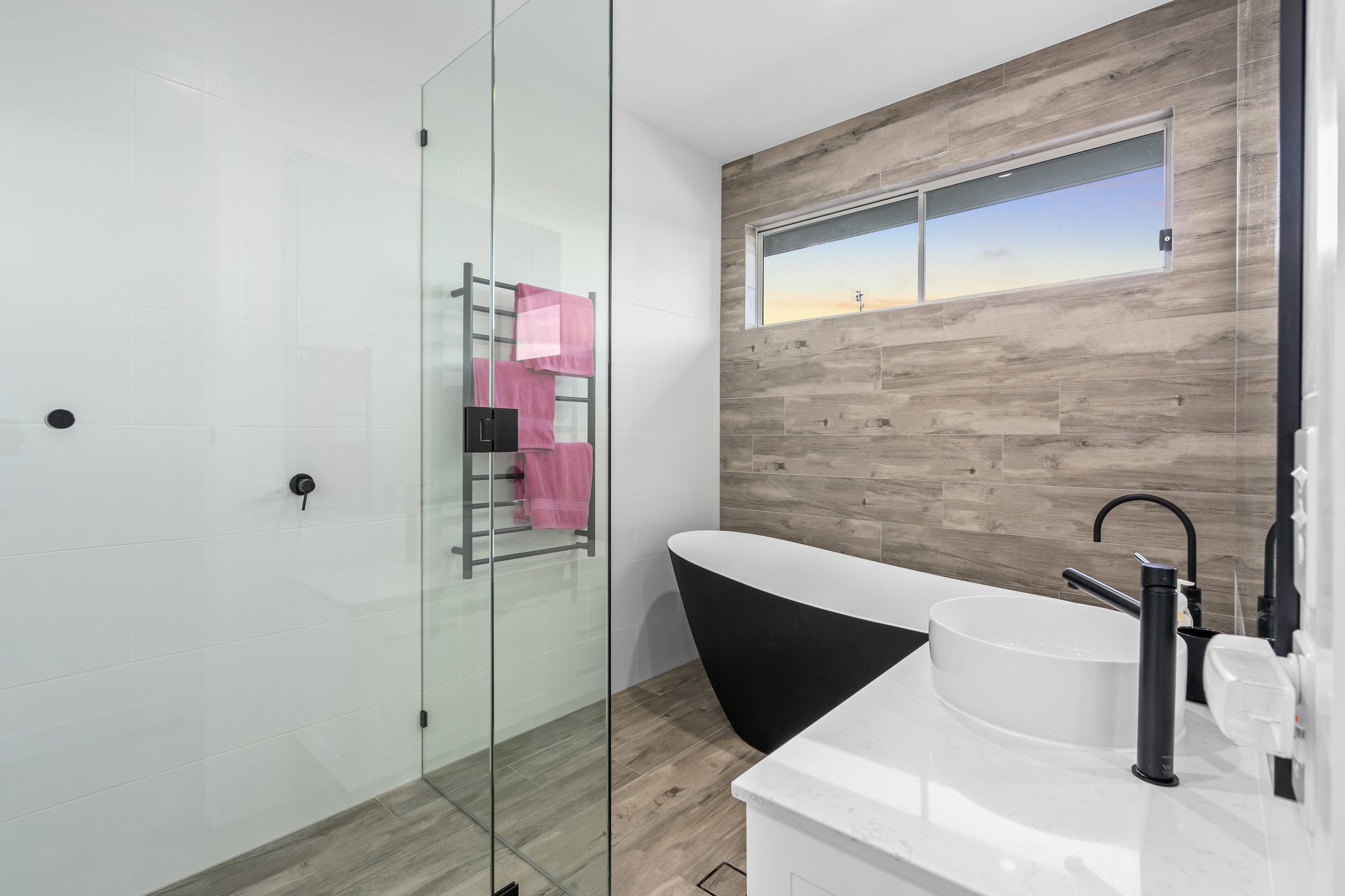 Bathroom with a freestanding black and white bath set against a timber-look tiled feature wall, beside a glazed shower.